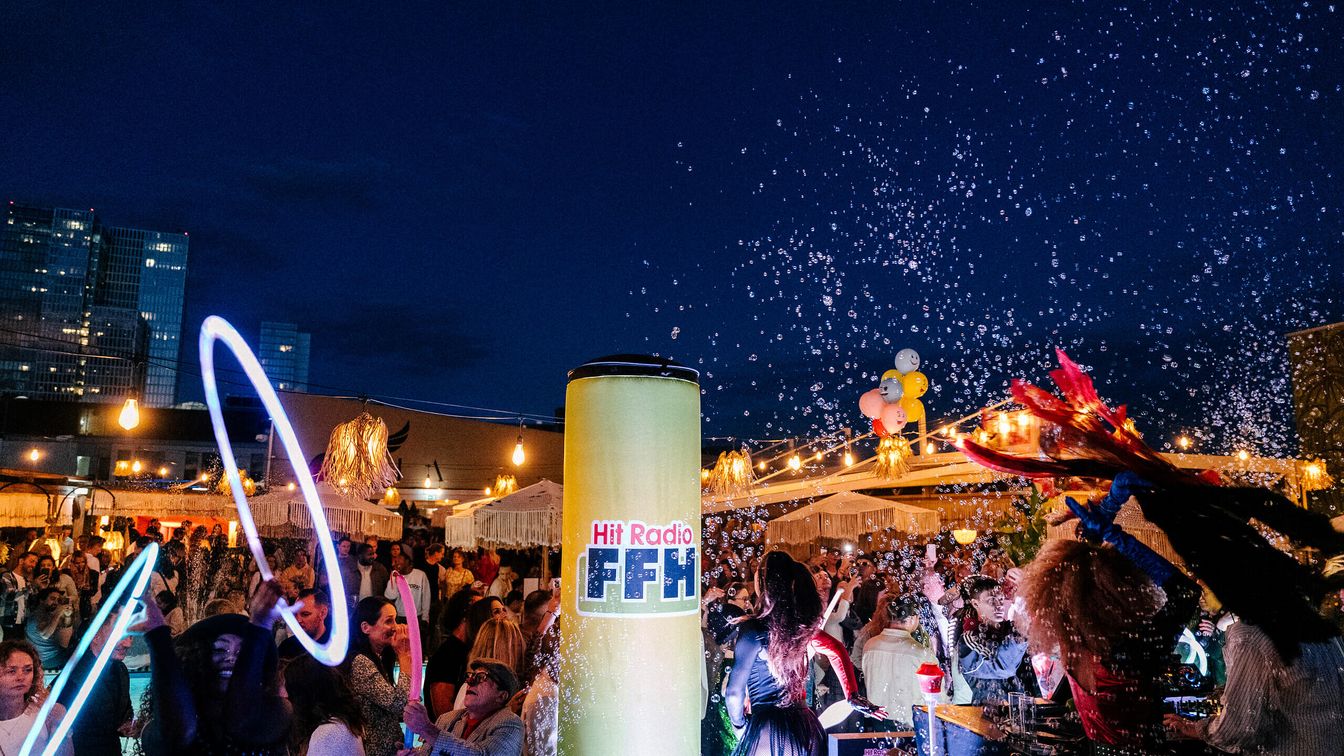 Nachtparty auf einer Dachterrasse mit Lichtern und Menschenmengen. 