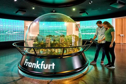 Ein Paar schaut auf eine mannshohe Glaskugel, die verschiedene Perspektiven von Frankfurt zeigt