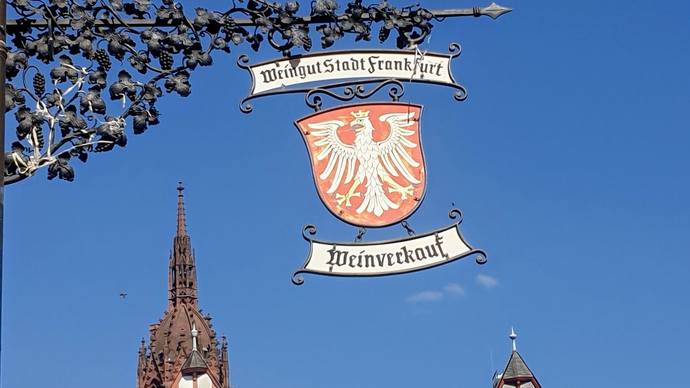 Schild des Weinguts Frankfurt mit Adlerwappen, Altstadt im Hintergrund.