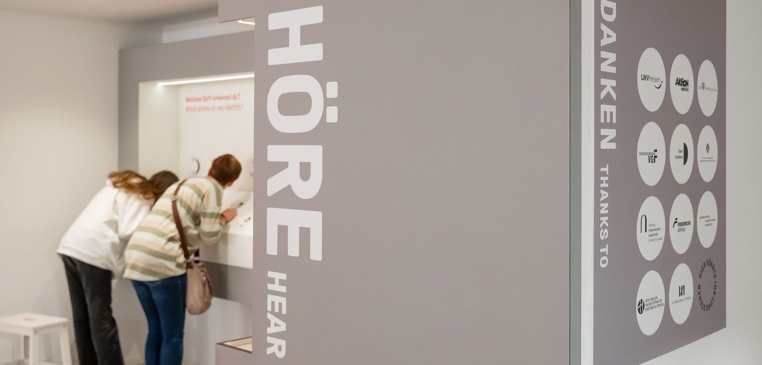 Zwei Personen betrachten eine Ausstellung zum Thema Hören.