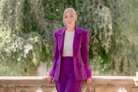 A woman in a purple suit is standing outside against a green background.