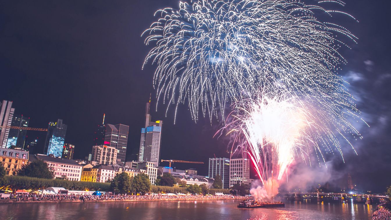 Ein spektakuläres Feuerwerk über dem Main in Frankfurt während des Abschlusses des Museumsuferfestes, mit glitzernden Lichtern und Menschen, die das Ereignis entlang des Flusses beobachten.
