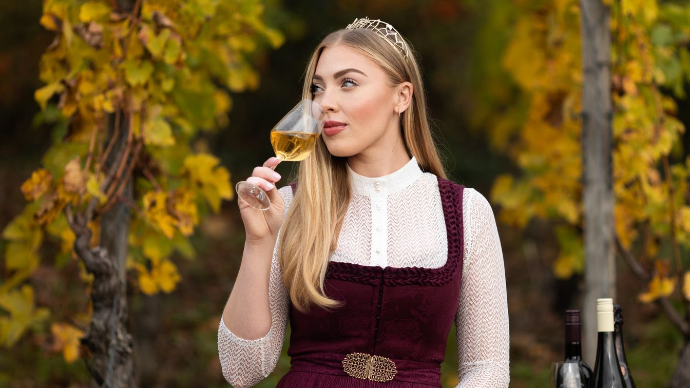 Frau mit Weinglas im Weinberg, herbstliche Reben im Hintergrund.
