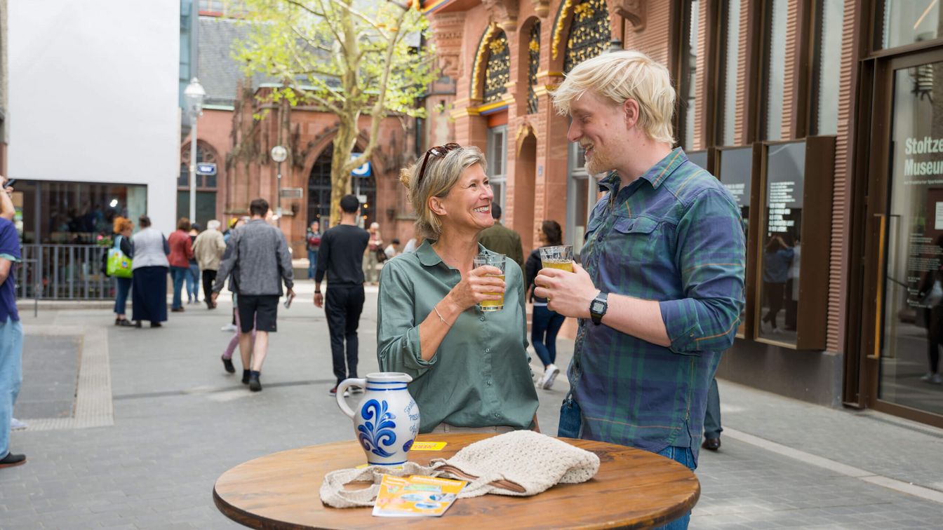 Ein Paar in der Neuen Altstadt schaut sich an und hält dabei gefüllte Gläser mit Apfelwein in der Hand