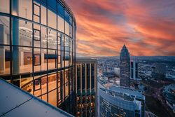 Glasfassade eines Hochhauses mit Blick auf Frankfurts Skyline bei Sonnenuntergang.