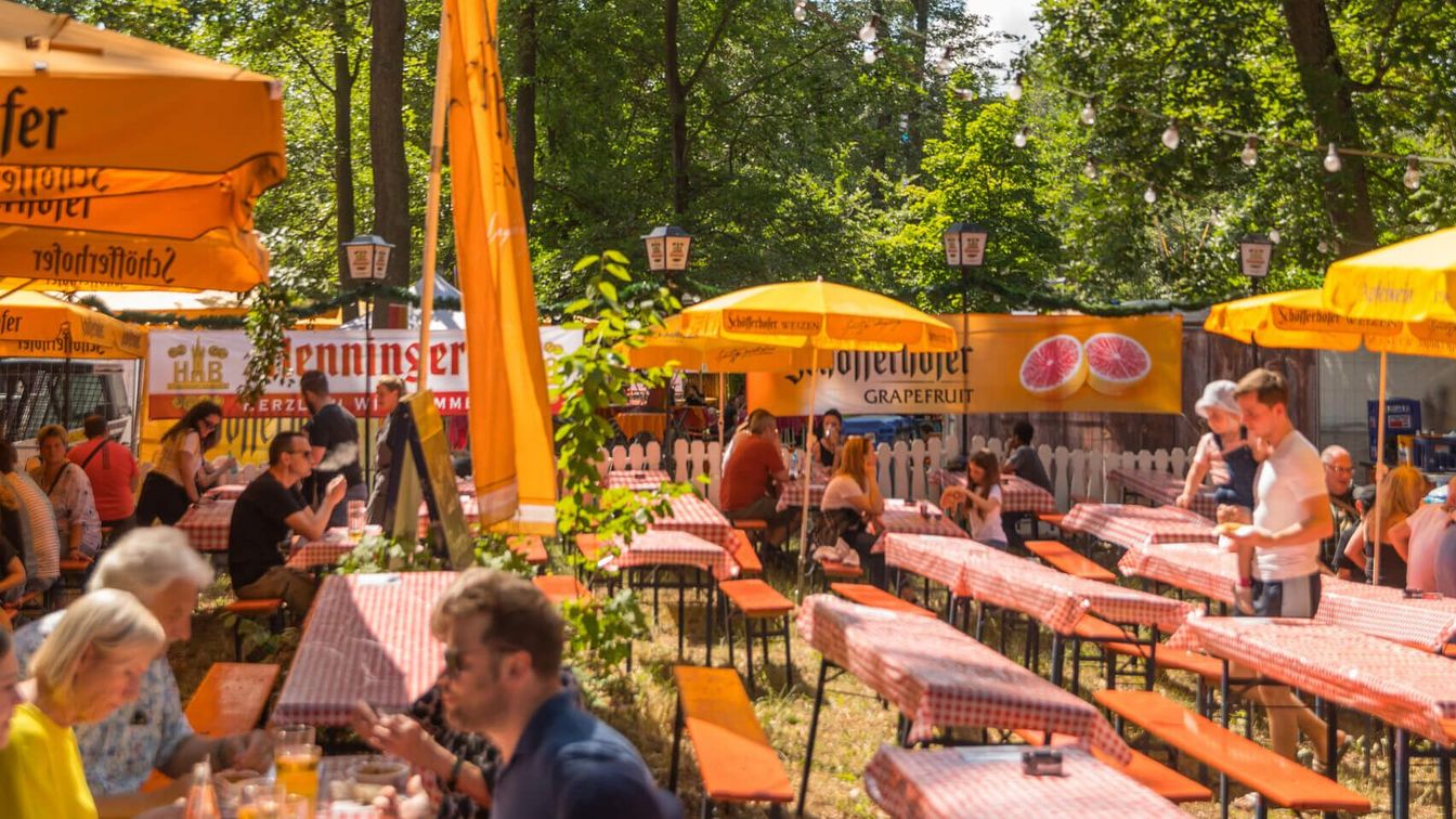 Gäste sitzen auf Bierzeltgarnituren an einem gastronomischen Stand beim Wäldchestag