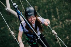 Woman with climbing gear in ropes course, smiling at the camera