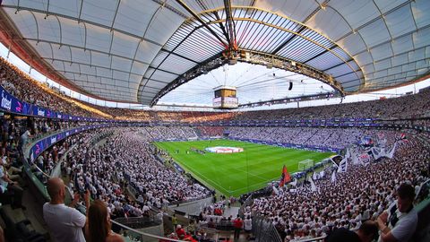 Das vollbesetzte Deutsche Bank Park Stadion während eines Fußballspiels. Tausende Fans in Weiß jubeln, das Spielfeld leuchtet unter dem beeindruckenden, überdachten Stadiondach.