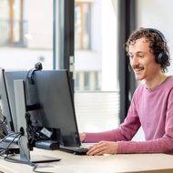 Ein Mann sitzt an einem Computer und spricht mit jemandem am Telefon. 