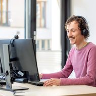 A man is sitting at a computer and talking to someone on the phone. 