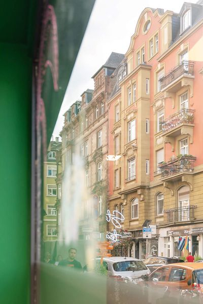Reflektion farbenfroher Altbaufassaden im Schaufenster eines modernen Geschäftes im Brückenviertel, mit Autos und urbanem Flair im Straßenbild.