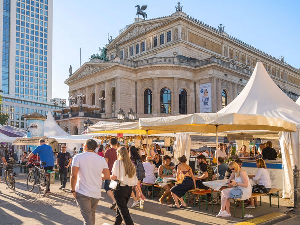 Menschen flanieren und sitzen beim Opernplatzfest vor der Alten Oper in Frankfurt. Die Stände und Sonnenschirme laden zum Verweilen ein.