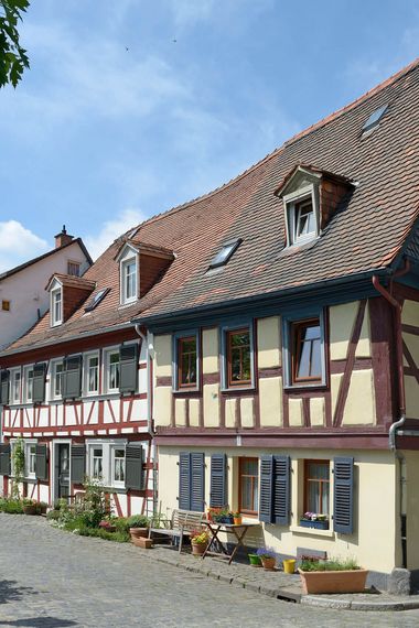 Reihe von kleinen Fachwerkhäusern in verschiedenen Farben in Frankfurt Höchst, Bänke und Blumen vor den Fenstern.