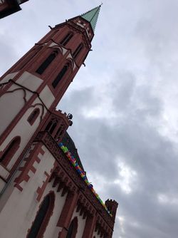 Kirchturm mit bunten Luftballons an der Brüstung unter bewölktem Himmel.