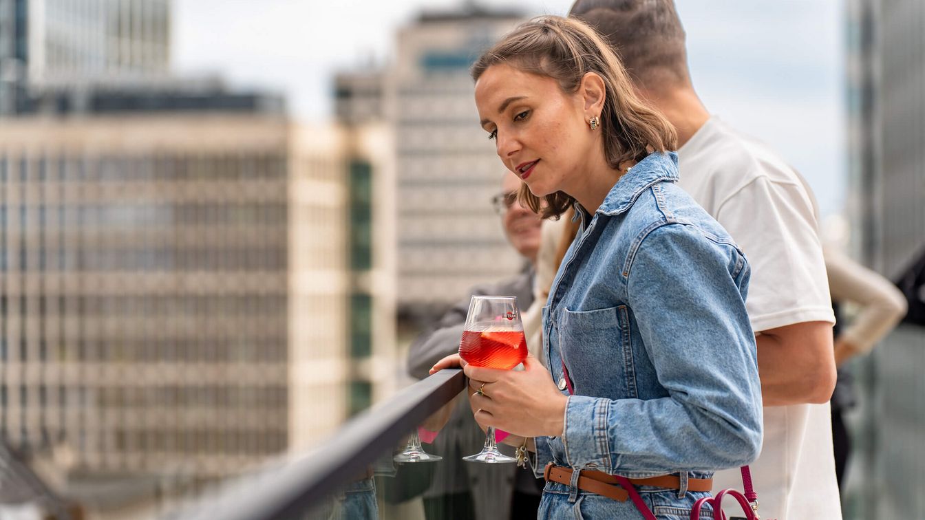 Frau mit Getränk genießt die Aussicht von einer Dachterrasse. 