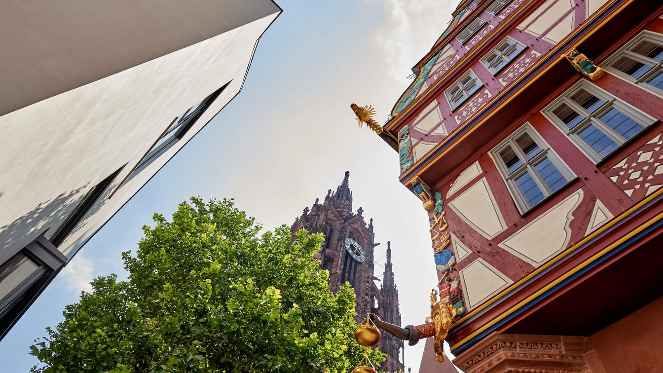 Blick in den blauen Himmel, zu sehen ist ein architektonischer Stilmix aus dem Fachwerkhaus Goldene Waage, dem Dom, einer weißen Hauswand.