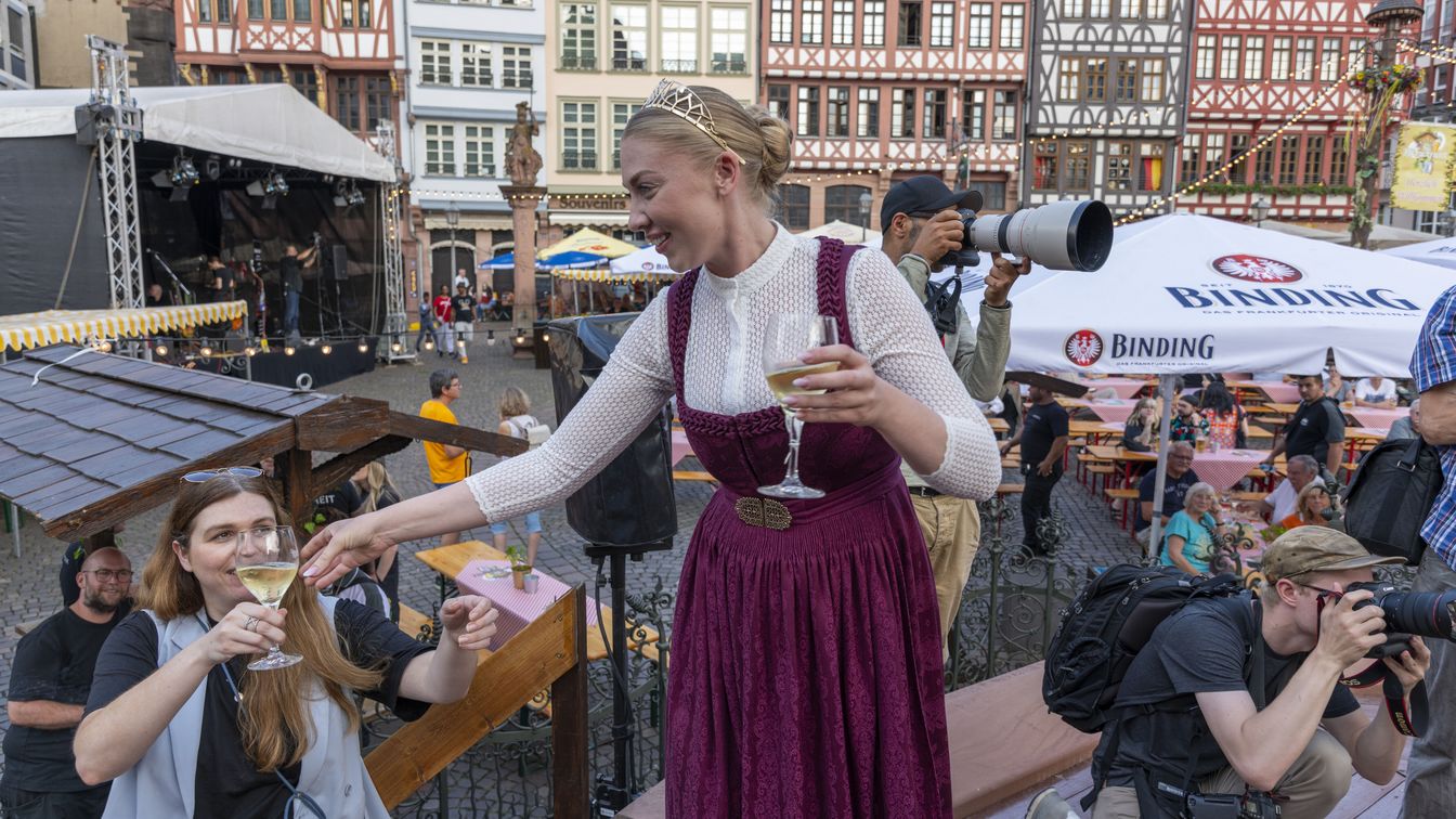 Frau reicht Weinglas an Besucherin bei Fest auf dem Frankfurter Römerberg.