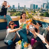 Eine Gruppe von Freunden stößt ausgelassen mit ihren Cocktails an, im Hintergrund der Skyline