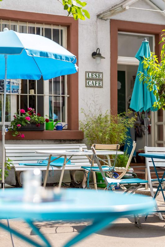 Gemütlicher Außenbereich eines Lesecafés in Frankfurt mit blauen Schirmen und Pflanzen.