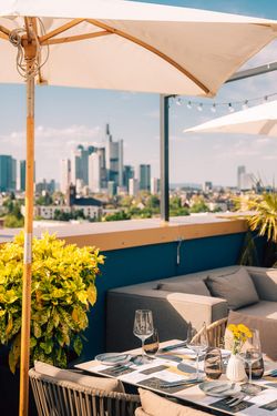 Edel eingedeckter Tisch in einer Rooftopbar mit Sonnenschirm und Blick auf die Skyline