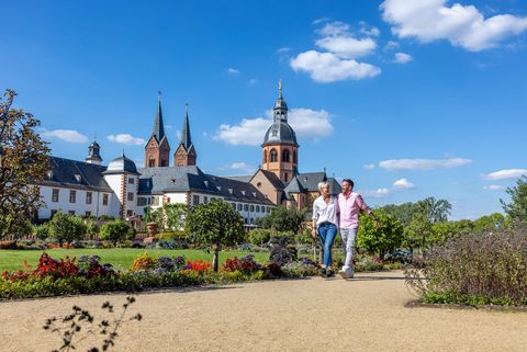 Fröhliches Paar läuft Arm in Arm durch den Klostergarten mit dem Kloster Seligenstadt im Hintergrund
