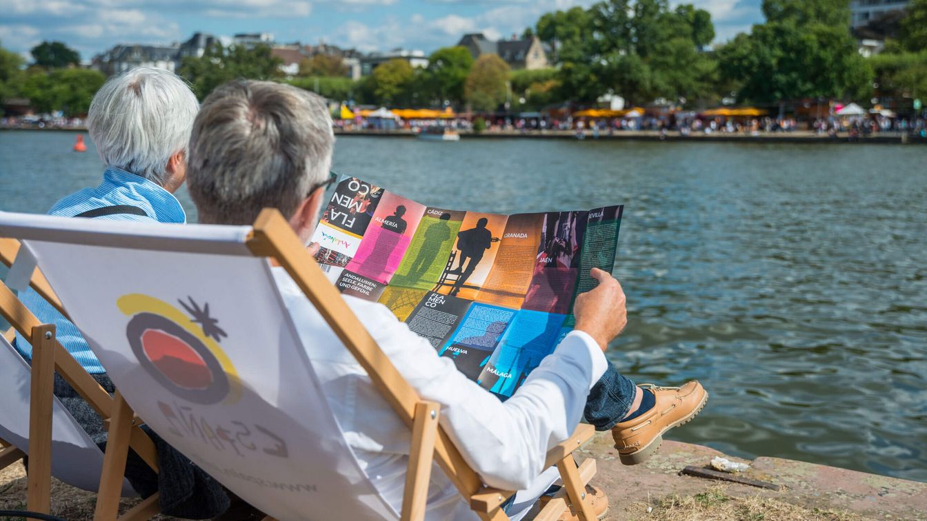 A couple sits in deckchairs on the banks of the Main and relaxes. 