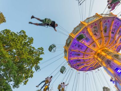 Ein Kettenkarussell beim Frankfurter Wäldchestag leuchtet bunt bei Dämmerung. Fahrgäste schwingen hoch in der Luft, während der Himmel sich sanft verfärbt.
