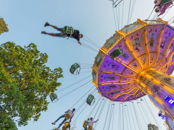 Ein Kettenkarussell beim Frankfurter Wäldchestag leuchtet bunt bei Dämmerung. Fahrgäste schwingen hoch in der Luft, während der Himmel sich sanft verfärbt.