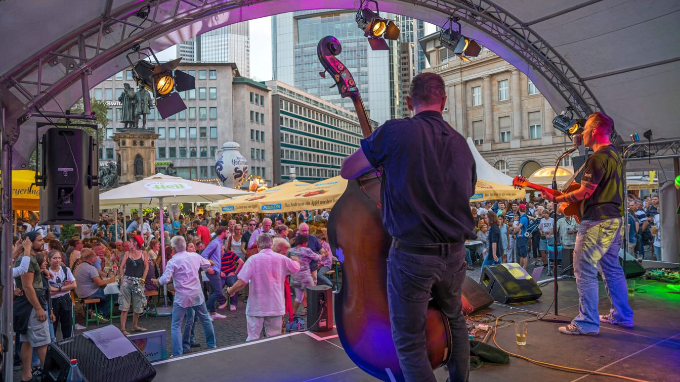 Musikbühne mit Künstlern und vor der Bühne befinden sich tanzende Menschen