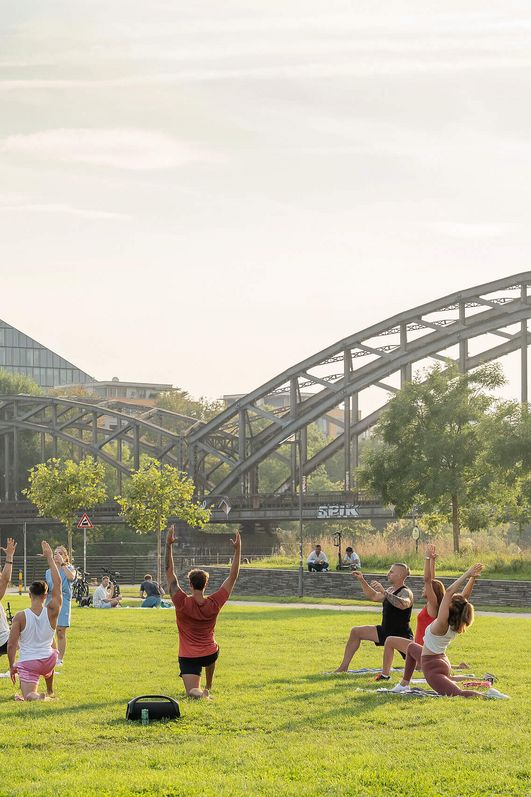 Menschen auf einer Wiese vor der EZB und der Osthafenbrücke in Frankfurt.