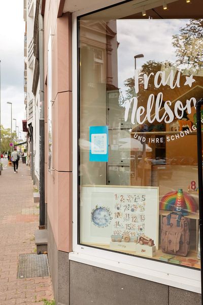 Die Fassade eines Geschäftes im Frankfurter Brückenviertel mit buntem Schaufenster. Die umliegende Straße ist geprägt von stilvollen historischen Gebäuden.