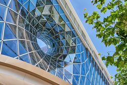Glasfassade des Einkaufszentrums MyZeil in Frankfurt, mit Bäumen und blauem Himmel.