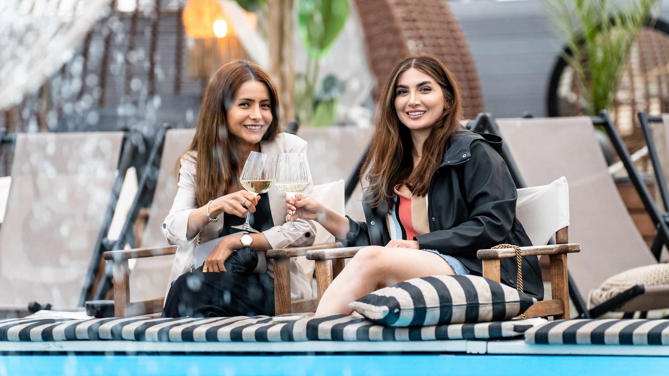 Zwei Frauen stoßen auf einer sommerlichen Lounge-Terrasse mit Weißwein in Frankfurt an.