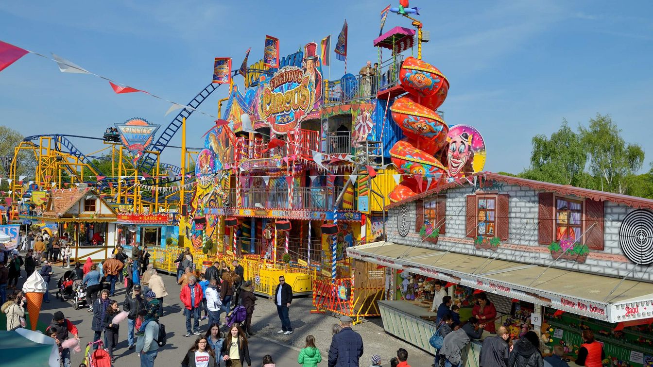 Gäste stehen auf dem Festgelände vor einem Fahrgeschäft namens Circus 