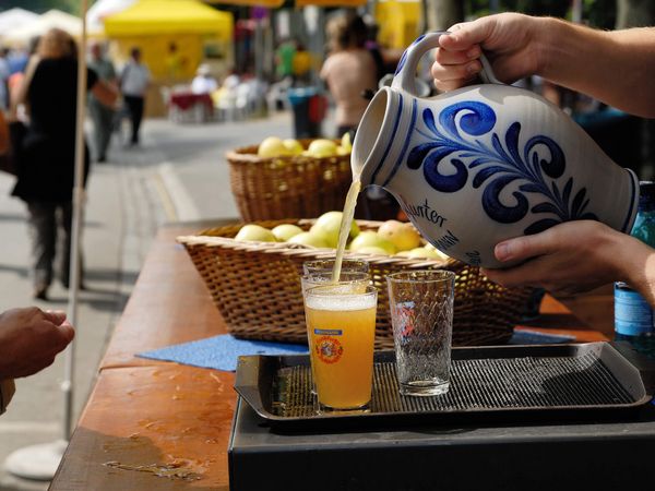 Apfelwein wird an einem Getränkestand aus einem Tonkrug, einem Bembel, in Apfelweingläser gefüllt