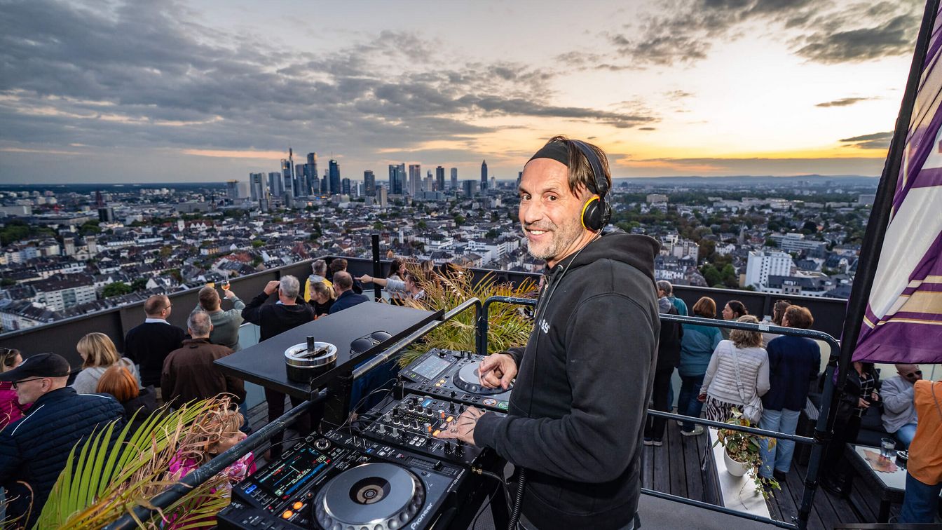 DJ spielt Musik auf einer Dachparty mit Stadtblick bei Sonnenuntergang. 