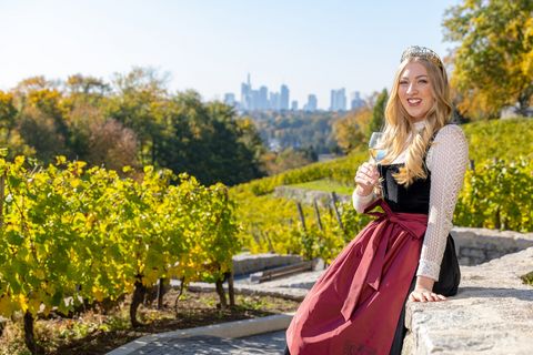 Frau mit Weinglas im Weinberg, Skyline von Frankfurt im Hintergrund.