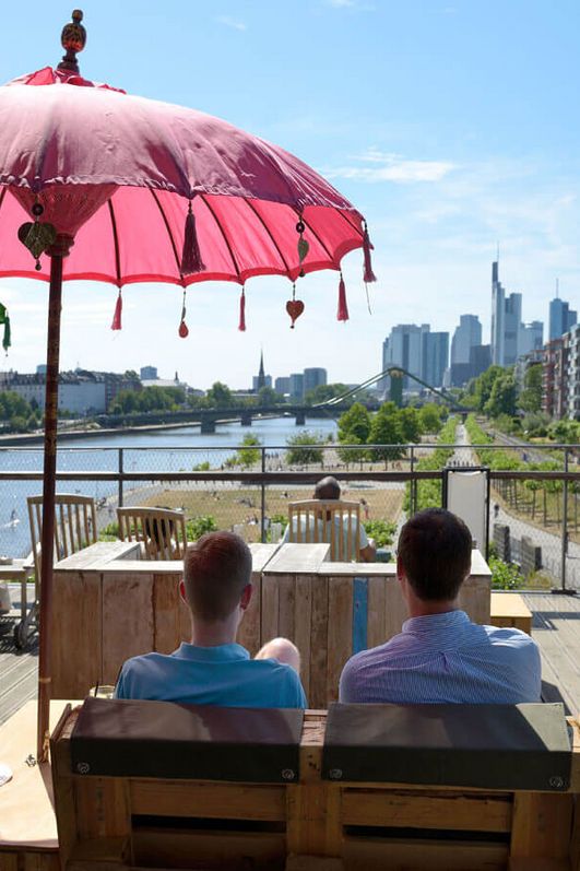 Zwei Männer sitzen unter einem Sonnenschirm und auf den Fluß Main und die Skyline