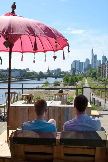 Zwei Männer sitzen unter einem Sonnenschirm und auf den Fluß Main und die Skyline