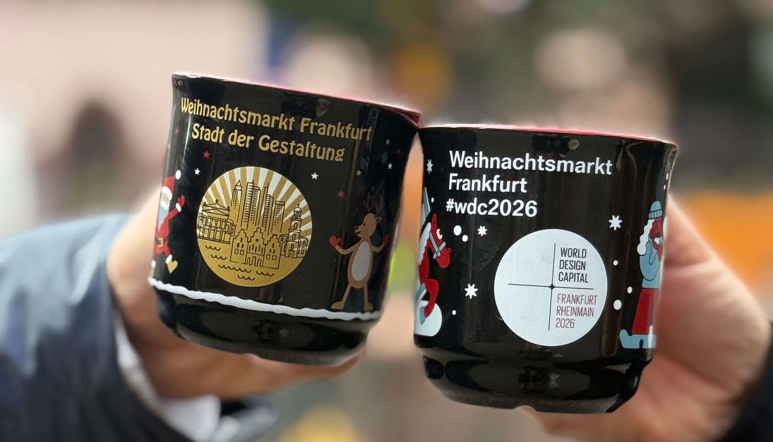 Two people clink black mulled wine mugs at the Frankfurt Christmas Market.