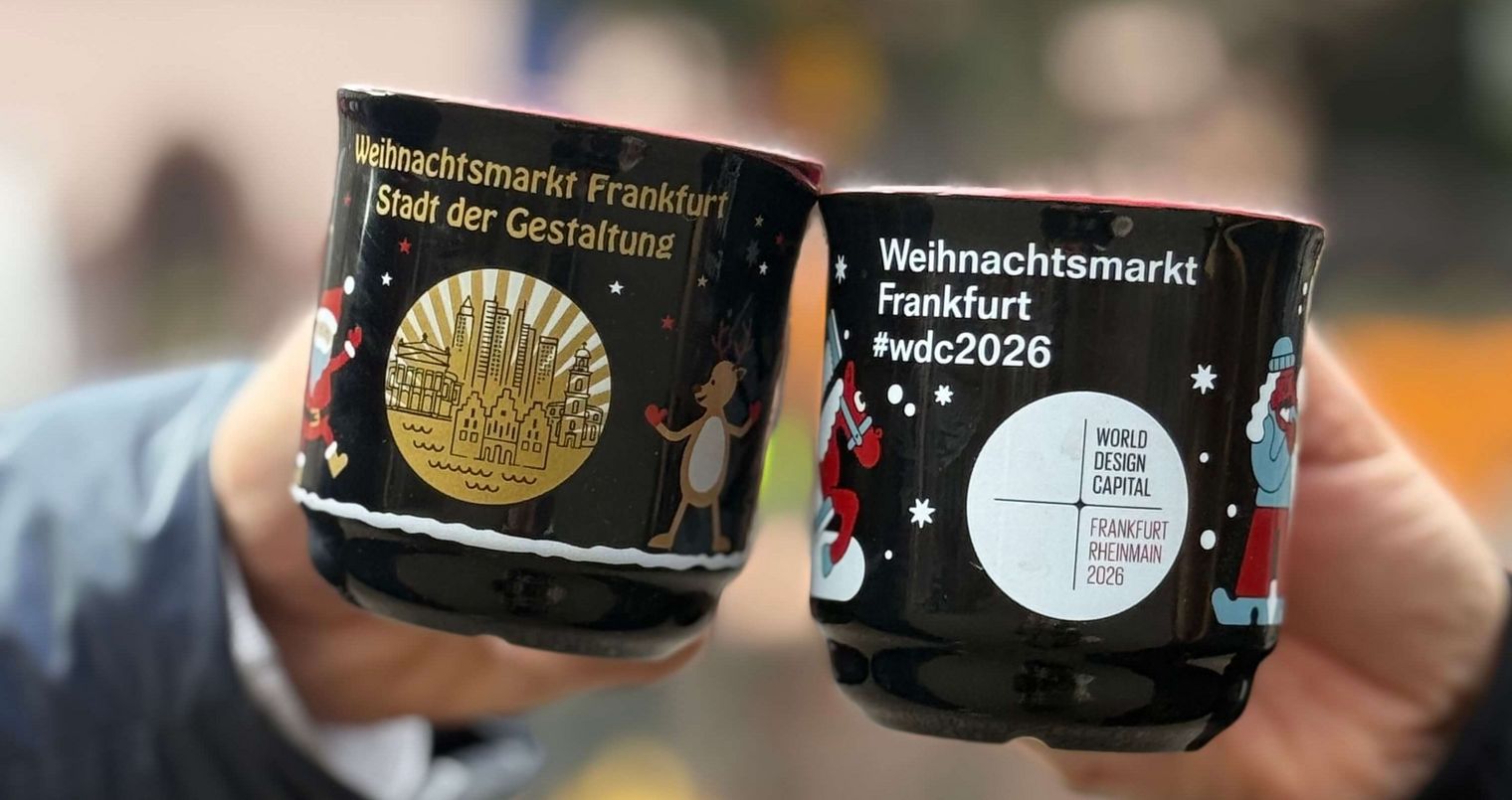 Zwei Personen stoßen mit schwarzen Glühweintassen des Frankfurter Weihnachtsmarkts an.