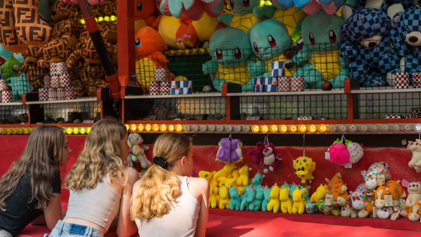 Children stand at a can throwing stand and look at the prizes. 