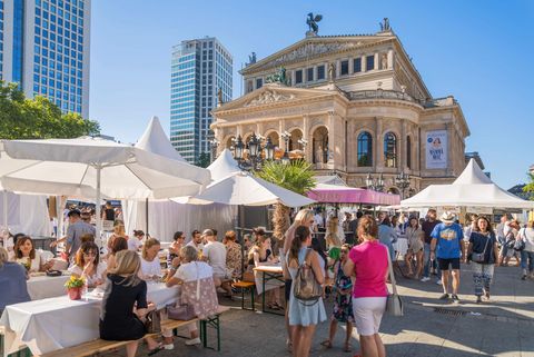 People enjoy the summer opera square festival in front of the Alte Oper in Frankfurt. Tents, benches and stalls create a lively atmosphere.