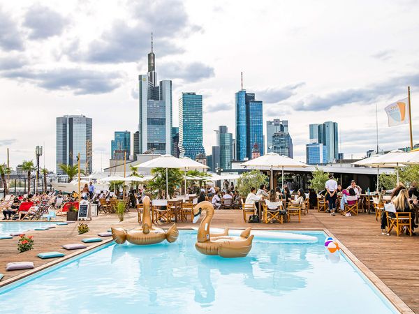 Rooptop Bar mit Pool, Sitzplätzen mit Sonnenschirmen und der Skyline im Hintergrund. 