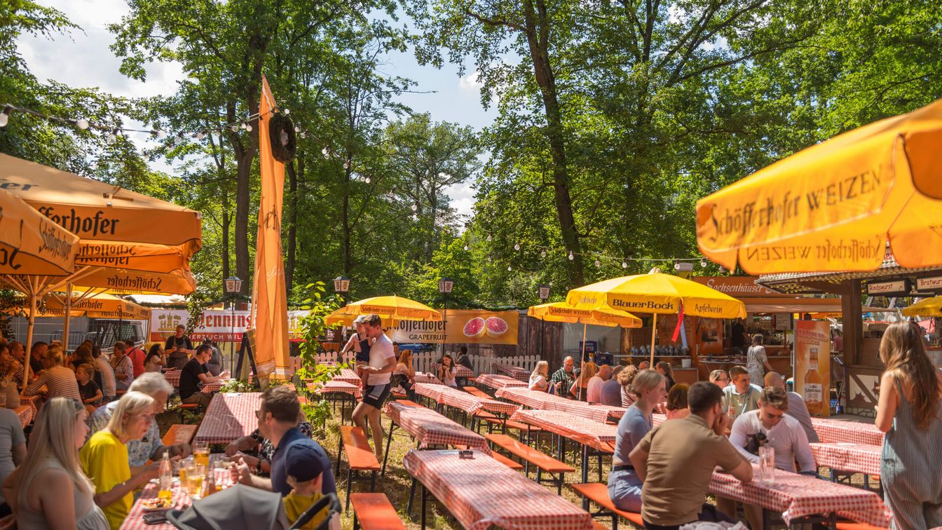 Gäste sitzen auf Bierzeltgarnituren an einem gastronomischen Stand beim Wäldchestag