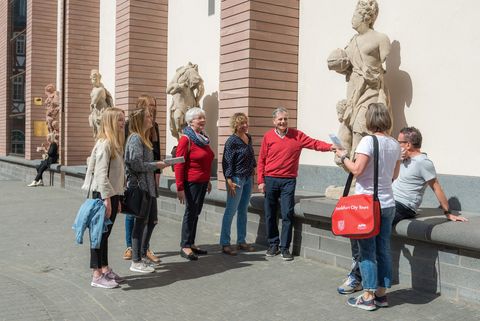 Eine Gruppe steht während eines Stadtrundgangs vor einer Statue vor dem Historischen Museum