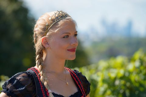 Frau mit Zopf und Krone im Profil, Reben und Skyline im Hintergrund.