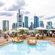Rooptop Bar mit Pool, Sitzplätzen mit Sonnenschirmen und der Skyline im Hintergrund. 