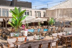 Ein stilvoller Rooftop-Beachclub mit Pool, Sonnenliegen, Holzmöbeln, Makramee-Schirmen und tropischen Pflanzen – ein perfekter Ort für entspannte Sommerabende und Cocktails unter freiem Himmel.