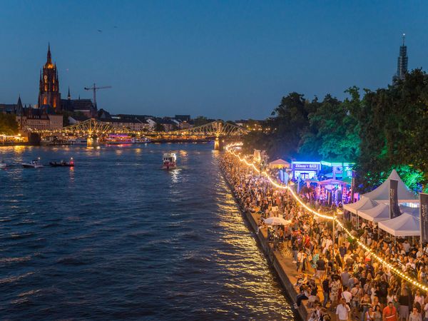 Besucher*innen bei Nacht auf dem beleuchteten Museumsuferfest, umgeben von Zelten und festlicher Atmosphäre.